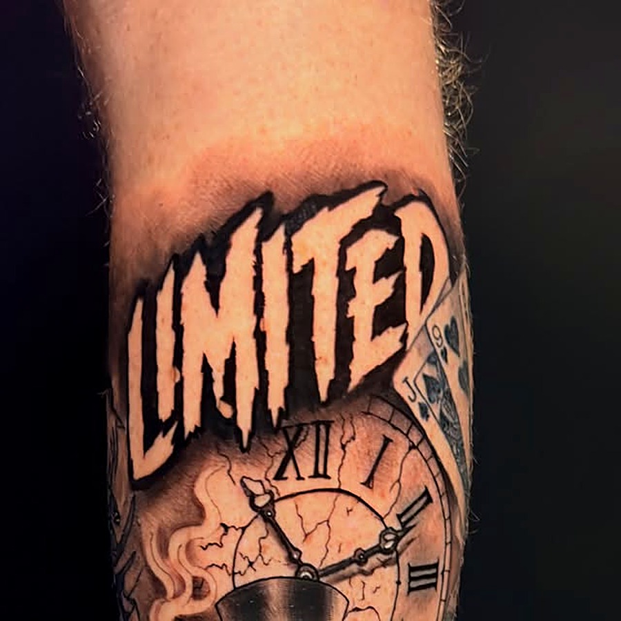 Black and grey tattoo — bold lettering over a cracked clock and playing card